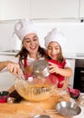 Happy mother baking with little daughter in apron and cook hat preparing dough at kitchen Royalty Free Stock Photo