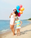 Happy mother and child with colorful balloons walking on beach Royalty Free Stock Photo