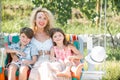 Happy mother and child swinging outdoor. Young mother with little kids son and daughter sitting on swing in summer park Royalty Free Stock Photo