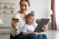 Happy mother with child using digital tablet and credit card, purchasing in internet, sitting on floor in living room Royalty Free Stock Photo