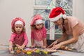 Happy mother and children identical twin daughters bake kneading dough in the kitchen, young family preparing christmas cookies Royalty Free Stock Photo