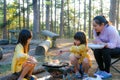 Happy mother and children picnic sit by stove near tent and grill a barbecue in pine forest, eating and have conversation. Happy