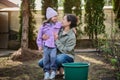 Happy mother and daughter enjoying gardening in the backyard of their country house, watering baby plants in the looseness ground