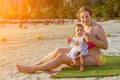 Happy mother with daughter enjoys sunbathing on the sandy tropical beach. Sunny warm day. Smiling baby with mom outdoors Royalty Free Stock Photo