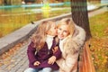 Happy mother with daughter have a rest sitting in autumn park on a bench. Royalty Free Stock Photo