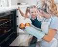 Happy mother and daughter removing muffins from the oven. Little girl looking at her parent holding a tray of muffins