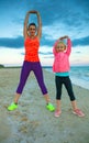 Happy mother and daughter on seacoast in evening stretching