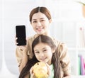 Happy mother and daughter showing the mobile phone and piggy bank Royalty Free Stock Photo