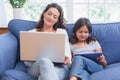 Happy mother and daughter sitting on the couch while using laptop and tablet Royalty Free Stock Photo