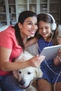 Happy mother and daughter sitting with pet dog and listening to music on headphones Royalty Free Stock Photo