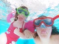 Happy mother and daughter sticking out their tonge, swim underwater in a swimming pool. Holidays and vacations, summer time.