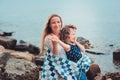 Happy mother and daughter wrapped in quilt blanket spending time together on the beach on summer vacation. Happy family traveling Royalty Free Stock Photo