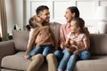 Happy mother and father with little daughters sitting on couch Royalty Free Stock Photo