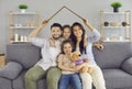 Happy mother and father sitting on a couch and holding a roof above their children Royalty Free Stock Photo