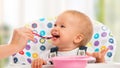 Happy mother feeds funny baby from spoon