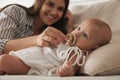 Happy mother giving pacifier to her cute little baby on sofa at home Royalty Free Stock Photo