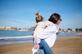 Happy mother giving piggyback ride to her lovely daughter, enjoying happy family time together on the Atlantic beach. Royalty Free Stock Photo