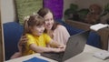 Happy mother helps baby girl daughter do homework computer together. mom strokes kid daughter head and smiles praises