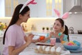 Happy mother with her cute daughter painting Easter eggs at table in kitchen Royalty Free Stock Photo