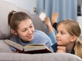 Happy mother with her daughter reading a book on the couch at home Royalty Free Stock Photo