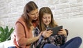 Happy mother and her daughter smiling having fun using digital tablet sitting on white sofa at home