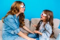 Happy mother and her little daughter in jeans clothes smiling to each other on couch  on blue background Royalty Free Stock Photo