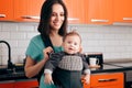 Happy Mother Holding Baby In Carrier in The Kitchen Royalty Free Stock Photo
