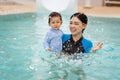 happy mother holding baby in her arms while playing water splashing in swimming pool