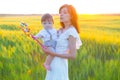 Happy mother holding baby smiling on wheat field in sunlight. Royalty Free Stock Photo