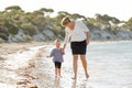 Happy mother holding hand of sweet blond little daughter walking together on sand at beach sea shore Royalty Free Stock Photo