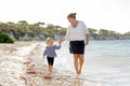 Happy mother holding hand of sweet blond little daughter walking together on sand at beach sea shore Royalty Free Stock Photo