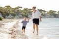 Happy mother holding hand of sweet blond little daughter walking together on sand at beach sea shore Royalty Free Stock Photo