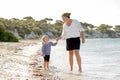 Happy mother holding hand of sweet blond little daughter walking together on sand at beach sea shore Royalty Free Stock Photo