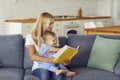 Happy mother holding her baby boy on knees and reading book together at home on sofa Royalty Free Stock Photo