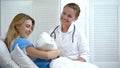 Happy mother holding newborn baby, smiling doctor looking at child, motherhood