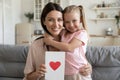 Happy mother holding postcard with drawn red heart embraces daughter Royalty Free Stock Photo