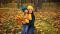 Happy mother hugs her cute little daughter in a beautiful autumn park with maples. Pretty mom in yellow wool knitted hat and Royalty Free Stock Photo