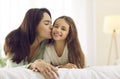 Happy mother kisses her pretty little daughter while cuddling together on a bed at home Royalty Free Stock Photo