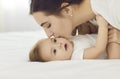 Happy mother kissing her baby girl on her soft little cheek while cuddling on bed together Royalty Free Stock Photo