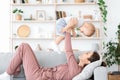 Happy mother lifting adorable toddler son in air while lying on couch