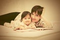 Happy mother and little baby girl reading a book on bed