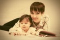 Happy mother and little baby girl reading a book on bed