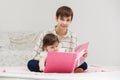 Happy mother and little baby girl reading a book on bed Royalty Free Stock Photo