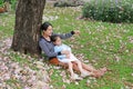 Happy mother and little child girl lying on green grass with fall pink flower in the garden outdoor. Asian mom pointing for her Royalty Free Stock Photo