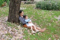 Happy mother and little child girl lying on green grass with fall pink flower in the garden outdoor. Asian girl pointing for her Royalty Free Stock Photo