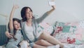 Happy mother and little girl taking selfie photo with smartphone camera and have fun grimacing while sitting in cozy bed Royalty Free Stock Photo
