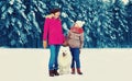 Happy mother looking at son child while walking with white Samoyed dog in snowy winter park on woods background Royalty Free Stock Photo