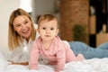 Happy mother lying with baby toddler on bed while kid girl crawling and looking at camera, playing in bedroom at home Royalty Free Stock Photo