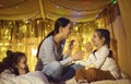 Happy mother playing with adorable cheerful children in home tent at evening