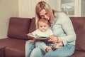 Happy mother read a book to child girl indoors sitting on couch Royalty Free Stock Photo